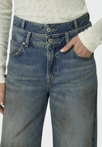 Denimjeans med hög midja i medelblått, utrustade med dubbla knappar och klassisk 5-fickdesign. Texturerat tyg med blekta områden.