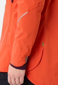 Giacca impermeabile arancione con un design elegante, dettagli riflettenti, una tasca laterale e orlo curvo.