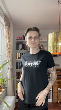 Černé bavlněné tričko s bílým logem "Levi's", krátkými rukávy a uvolněným střihem. Na pažích jsou viditelné výrazné tetování.