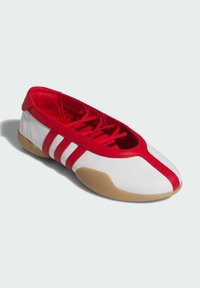 Crvene i bijele sportske cipele s fleksibilnim dizajnom, glatkim sintetičkim gornjim dijelom, crvenim vezicama sprijeda i potplatom od gumene gume.