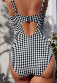 Schwarz-weiß karierten Badeanzug mit Ausschnitt am Rücken, verstellbaren Trägern und einem metallischen Verschlussdetail. Strukturierter Stoff.