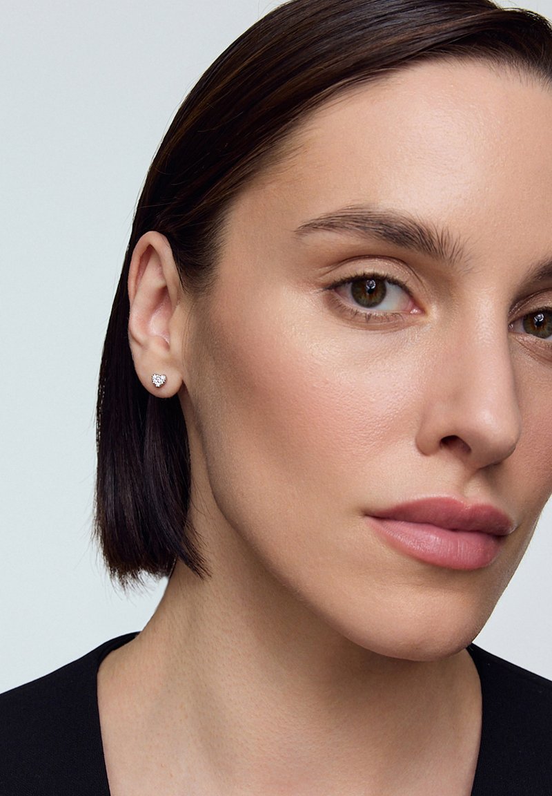 Srebrna kolczyk w kształcie serca na uchu modelki. Projekt charakteryzuje się delikatną formą i wypolerowanym wykończeniem, co podkreśla ogólną elegancję.