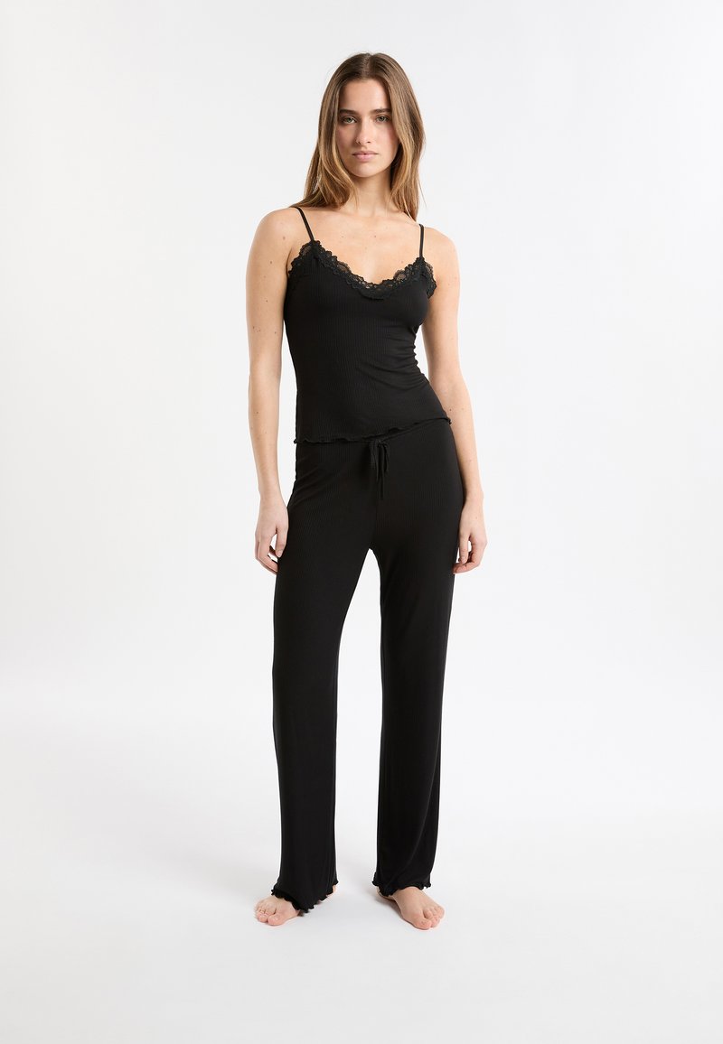 Conjunto de pijama negro acanalado que incluye una camiseta ajustada con detalle de encaje, tirantes ajustables y pantalones de corte holgado con dobladillos con volantes. Textura suave de la tela.