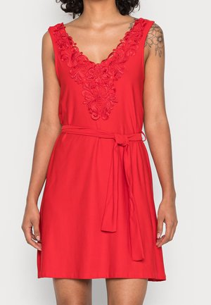 Robe sans manches rouge avec un décolleté en V profond, ornée de broderies florales au niveau du cou et d'un détail de taille à nouer. Texture de tissu lisse.
