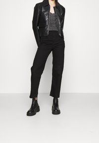 Giacca nera in pelle cropped con zip, top grigio testurizzato e pantaloni neri a vita alta. Completato con stivali neri chunky alla caviglia.