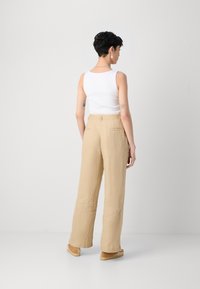 Beige linen wide-leg pants with a high waist, featuring side pockets and a smooth texture. Paired with a white ribbed tank top.