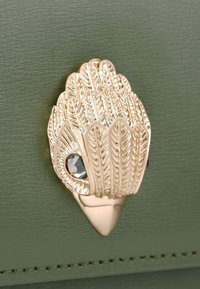 Materiale verde texturizzato con un accessorio in metallo a forma di foglia dorata che presenta una gemma sfaccettata. Il dettagliato motivo a foglia arricchisce il design.