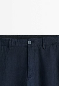 Marinblå linnebyxor med knappstängning, bältesöglor och en slät yta. Detaljerad sömnad vid fickorna och sömmarna.