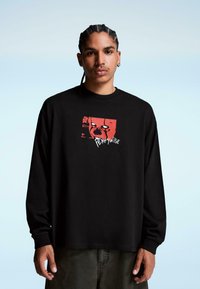 Tricou negru cu mânecă lungă, având un imprimeu grafic în roșu și alb, care ilustrează fața unui clovn cu textul "Pennywise" dedesubt. Material din bumbac.