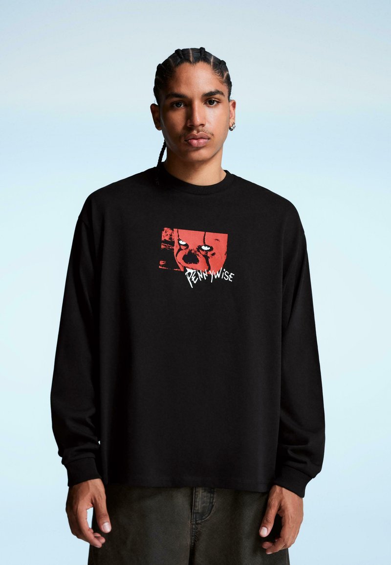 Tricou negru cu mânecă lungă, având un imprimeu grafic în roșu și alb, care ilustrează fața unui clovn cu textul "Pennywise" dedesubt. Material din bumbac.