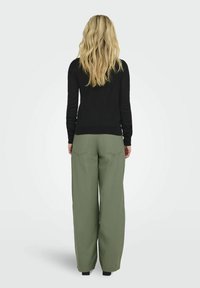 Schwarzer Pullover mit langen Ärmeln, kombiniert mit olivgrünen, weit geschnittenen Hosen. Auffällige Details sind die gerippten Bündchen und das schlichte Design.