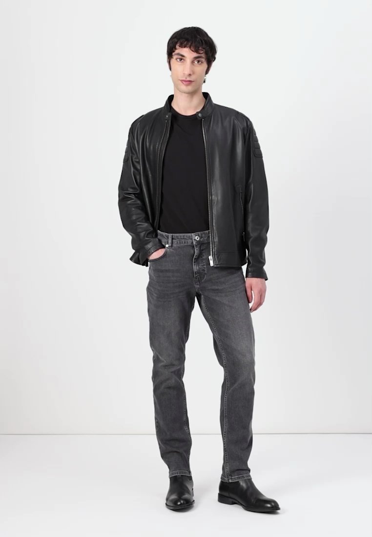 Veste bomber en cuir noir avec fermeture éclair, jeans gris avec un léger dégradé, et bottines noires. Le mannequin se tient devant un fond uni.