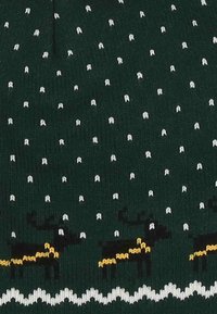 Gorro de punto en verde oscuro con lunares blancos, que presenta diseños de renos negros acentuados con detalles amarillos y una banda ondulada blanca en la parte inferior.