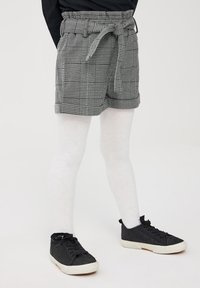 Shorts a quadri grigi con vita regolabile e orlo arrotolato, abbinati a collant bianchi e scarpe da ginnastica nere in tela. Tessuto strutturato con un design classico.