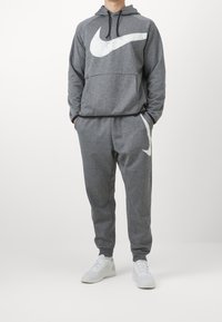 Ensemble sweat à capuche et pantalon de survêtement gris en tissu doux, avec un grand logo Nike blanc sur le devant et chaque jambe du pantalon. Style à capuche.