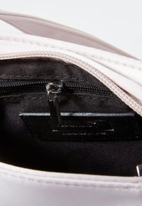 Interno di una borsa a mano rosa chiaro con rivestimento nero, dotato di una tasca con zip e di un'etichetta. Texture morbida, design elegante e chiusura semplice.