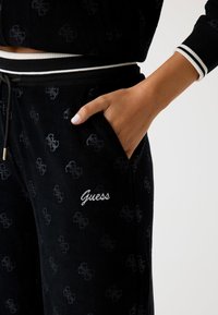 Zwarte corduroy joggers met een subtiel logopatroon, een elastische tailleband met witte streep en geborduurd "Guess" op de zak.