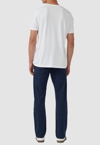 Witte katoenen t-shirt met korte mouwen, gepaard met donkerblauwe broek en witte schoenen. T-shirt heeft een eenvoudig ronde hals ontwerp.
