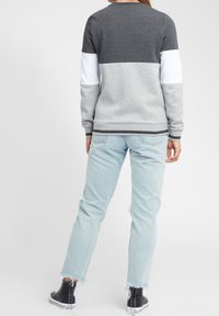 Sweatshirt grigio e bianco a blocchi di colore con colletto rotondo, polsini e orlo a costine. Abbinato a jeans chiari strappati e stivaletti neri.
