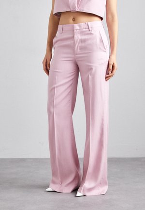 Pantalones anchos de color rosa claro, hechos de un tejido suave, con cintura alta y bolsillos delanteros, combinados con zapatos blancos de punta.