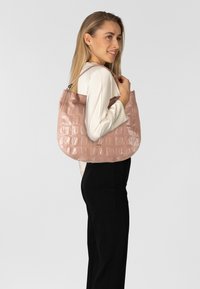 Lichtroze, glanzende nepleren handtas met krokodillenpatroon, een gebogen vorm en een enkele schouderriem. Geen zichtbare metalen details.