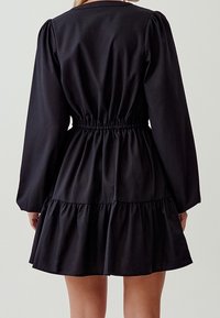 Abito nero con lunghe maniche a sbuffo, vita cinchata e orlo a strati e volants. Realizzato in tessuto morbido con un design semplice e pulito.