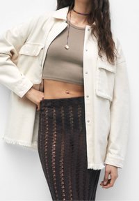 Kremowa przesadnie duża kurtka z postrzępionym dołem, dwie przednie kieszenie; brązowy prążkowany top do pępka; czarna dzianinowa spódnica w wzory z pionowymi pasami.