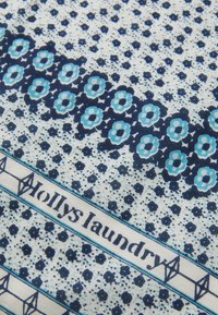 Bomullsstoff med hvit bakgrunn, med blå blomsterdesign, geometriske detaljer og teksten "Molly's Laundry" i marineblå.