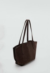 Bolso de tote de ante marrón con dos asas largas, que presenta un diseño simple y una textura suave, forma ligeramente estructurada y sin herrajes visibles.