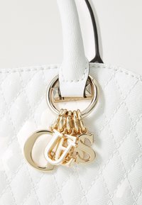 Borsa a tracolla bianca trapuntata con un accento in hardware dorato lucido e un charm che mostra le lettere "C," "U," e "S." Superficie testurizzata.