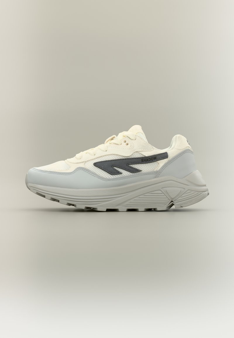 Tenisice s bijelim mrežastim gornjim dijelom, sivim kožnim detaljima i teksturiranim svijetlosivim đonom. Sadrže logotip i kontrastni tamnosivi dizajnerski element.