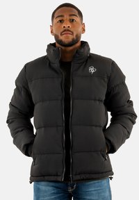 Veste en duvet noire avec un texture côtelée verticale, col haut, fermeture éclair sur le devant et poches latérales. Présente un petit logo blanc sur la poitrine.