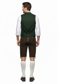 Gilet verde con design aderente, abbinato a pantaloni corti marroni. Camicia a maniche lunghe bianca sotto, completata da calze bianche fino al ginocchio.