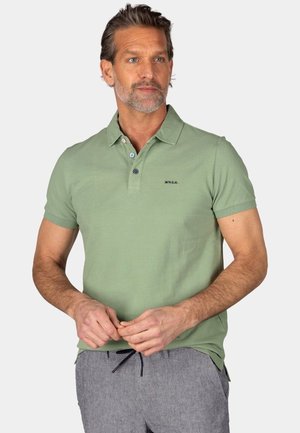 Groene polo met korte mouwen, drieknops sluiting en geborduurd logo. Draagt met grijs gestreepte broeken van soepele stof.