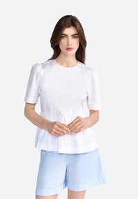 Hvid kortærmet top med rund halsudskæring, samlet talje og peplum-stil. Sammen med lyseblå shorts. Glat tekstur.