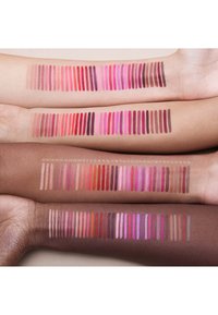 Drie armen tonen een reeks lipstiftstalen in tinten nude, roze en rood. De texturen variëren van mat tot satijn, met een consistente, gelijkmatige aanbreng.