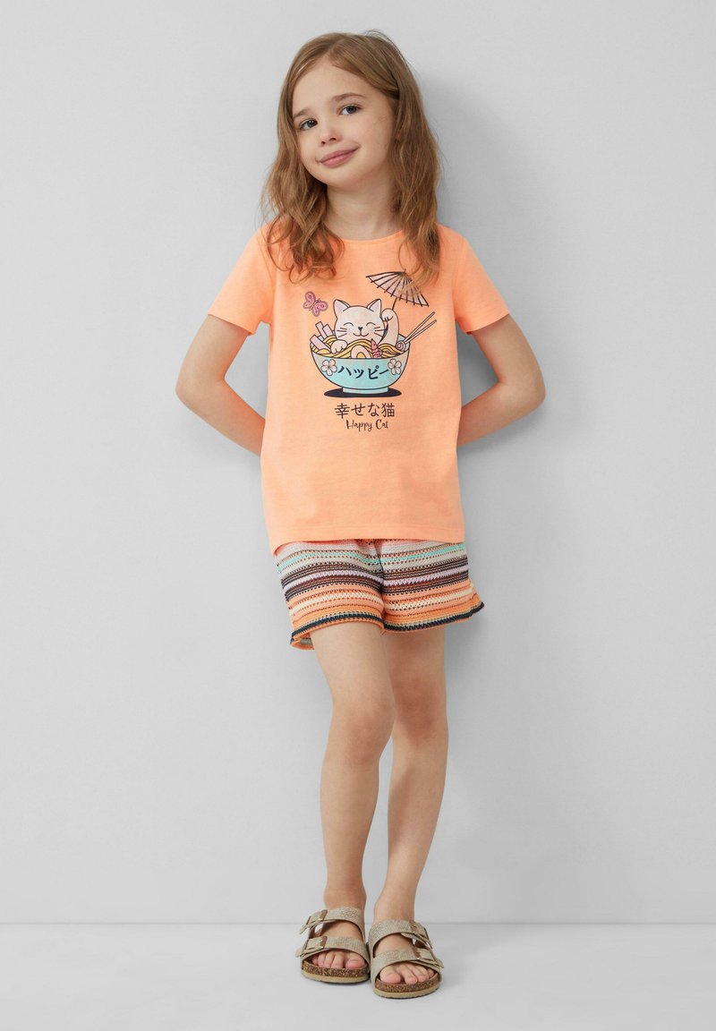 Felgekleurde oranje katoenen T-shirt met een cartoonkat in een kom noedels als afbeelding. Gecombineerd met kleurrijk gestreepte shorts en beige sandalen.