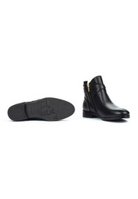 Botas de tobillo de cuero negro con tacón bajo, que cuentan con un cierre lateral, detalles de correas cruzadas y suela de goma texturizada con un patrón de estrellas.