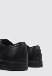 Zapatos de cuero negro con un acabado suave, puntera redonda, tacón bajo y un detalle de costura minimalista en la parte posterior, destacando un diseño clásico.