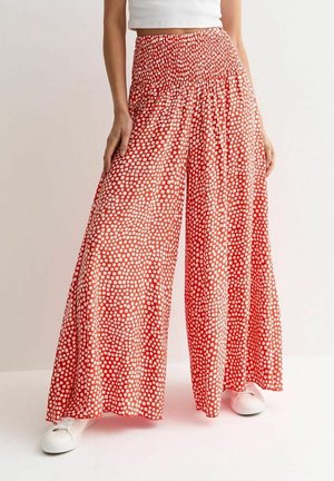 Mujer con pantalones anchos rojos con patrón de cuadros blancos y una camiseta corta blanca, combinados con zapatillas blancas.