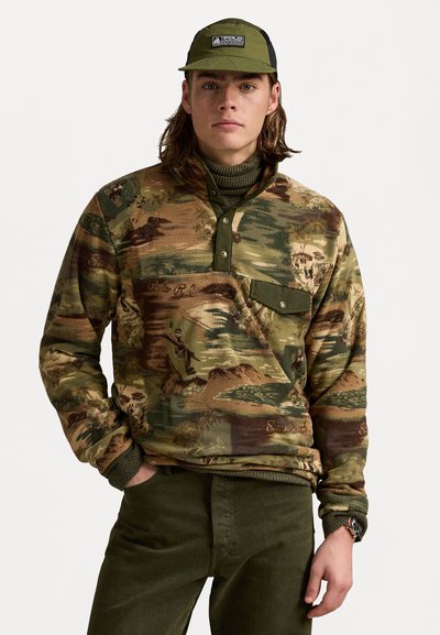 Sweat-shirt à motif camouflage dans des tons terre, avec un col montant, une patte de bouton et une poche poitrine; porté sur un turtleneck vert.