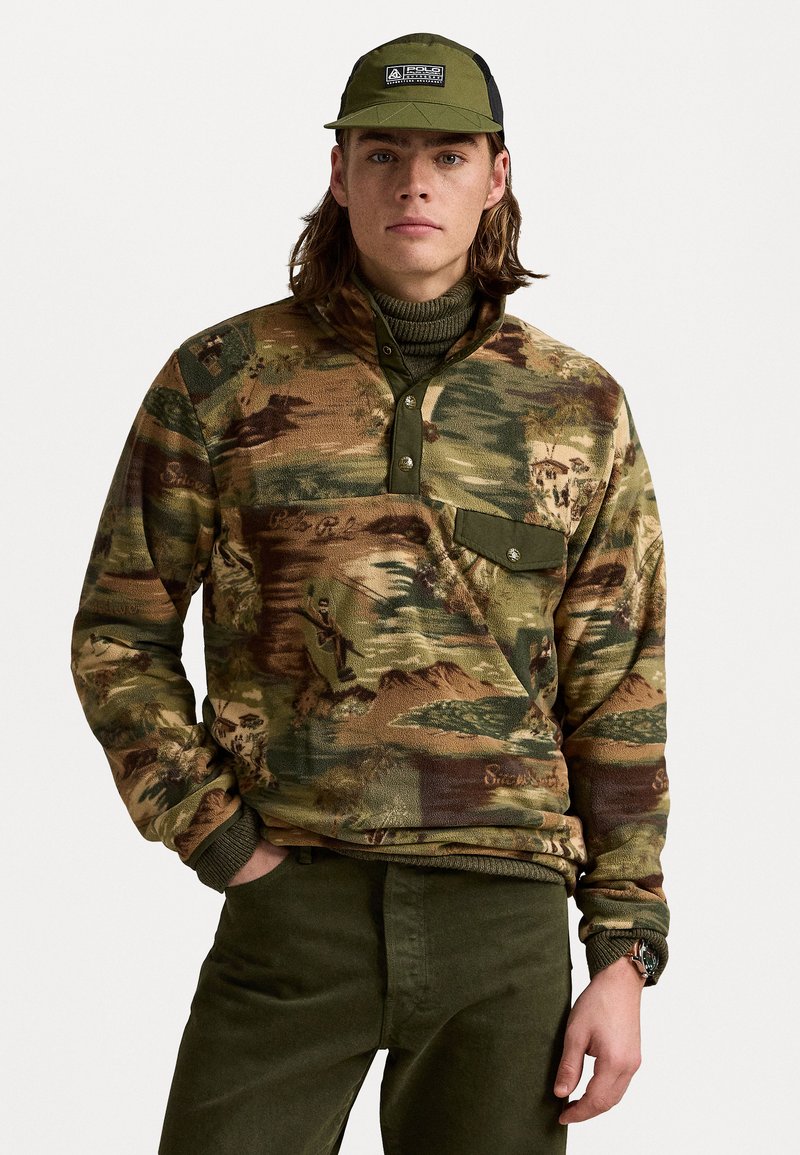 Camo-patterned pullover sweatshirt in earth tones with a high collar, button placket, and a chest pocket; worn over a green turtleneck.