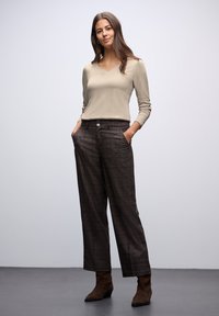 Beżowa bluzka z długim rękawem i dekoltem w serek, w połączeniu z brązowymi, w kratkę, spodniami z wysokim stanem oraz brązowymi botkami za kostkę, posiadającymi kieszenie boczne i dwa przednie guziki.