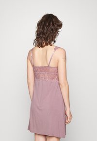 Roze nachthemd met kantdetails op de rug, dunne verstelbare bandjes, en een zachte, vloeiende stof die boven de knie valt.