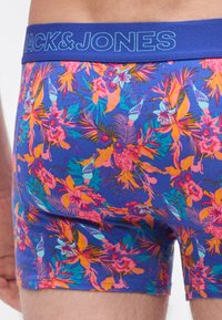 Herrenslips aus blauem Stoff mit einem bunten Blumenmuster in Pink, Orange und Grün; elastischer Bund mit "JACK & JONES"-Logo.