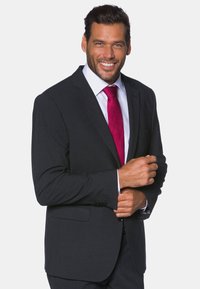 Giacca in suit grigio scuro con rever a punta e una tasca, indossata sopra una camicia bianca e una cravatta di un vivace rosa. Vestibilità su misura con texture morbida.