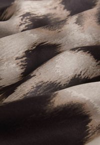 Stoff mit einem strukturierten Muster, das Nuancen von Braun und Beige zeigt und einen fließenden Fall mit sanften, welligen Falten erzeugt.