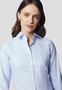 Jasnoniebieska koszula zapinana na guziki w paski, z klasycznym kołnierzykiem i długimi rękawami; zapięcie guzikiem z przodu; gładka tekstura materiału.