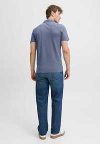 Herren Poloshirt mit kurzen Ärmeln in Hellblau, kombiniert mit lockeren blauen Denim-Jeans und weißen Sneakers, von hinten betrachtet.