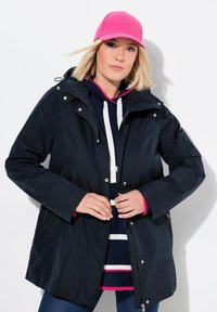 Marintröja vattentät med huva, tryckknappar och dold dragkedja. Matchad med en randig hoodie i marinblått och vitt samt en rosa keps.